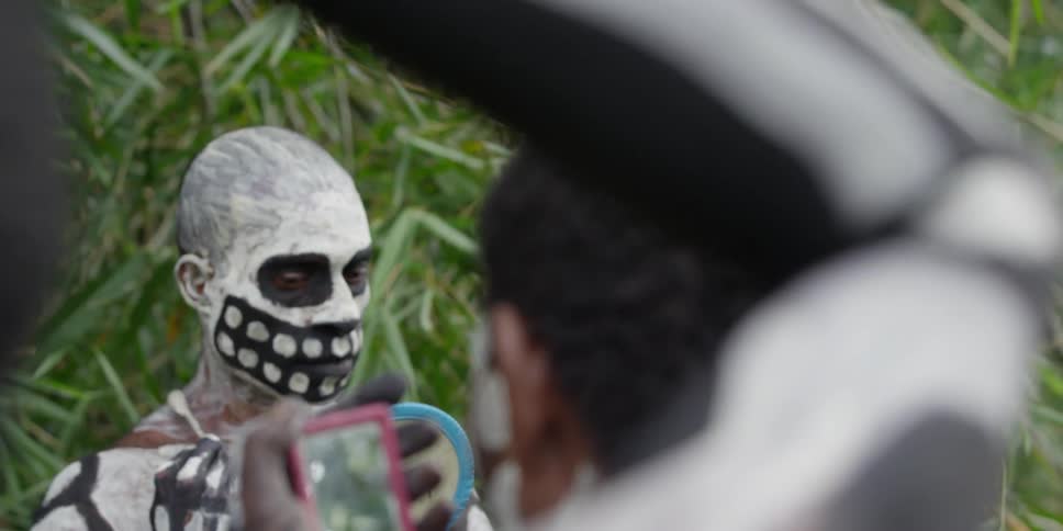 Native men look in hand mirrors while painting their faces