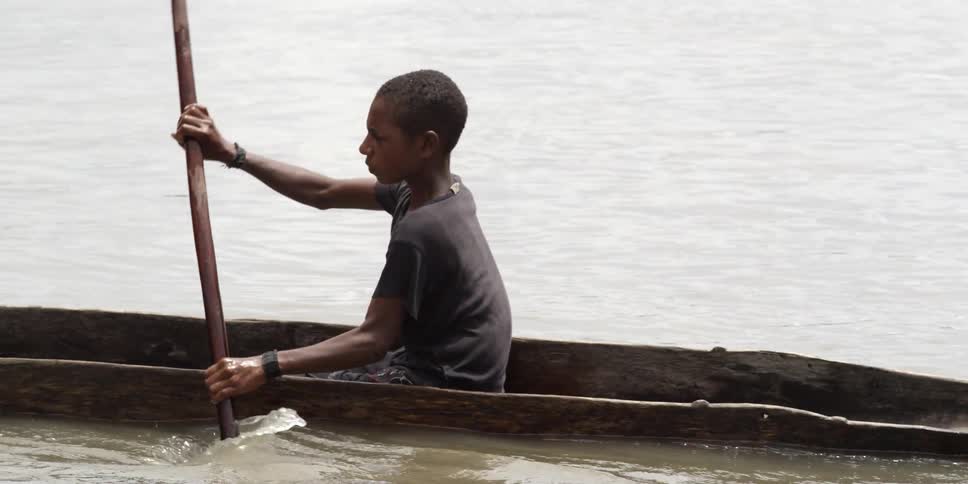 A young man rowing a canoe carved from a tree trunk