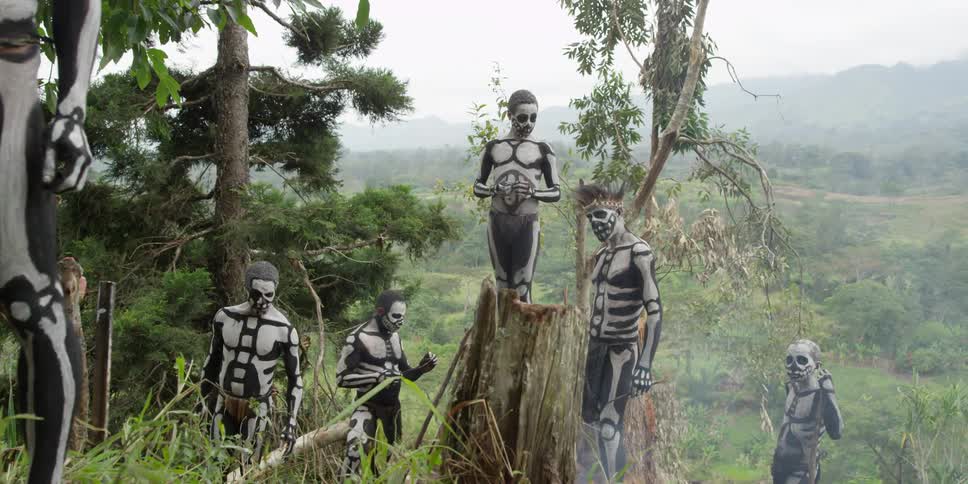 A group of indigenous people in skeleton paint stand in the forest
