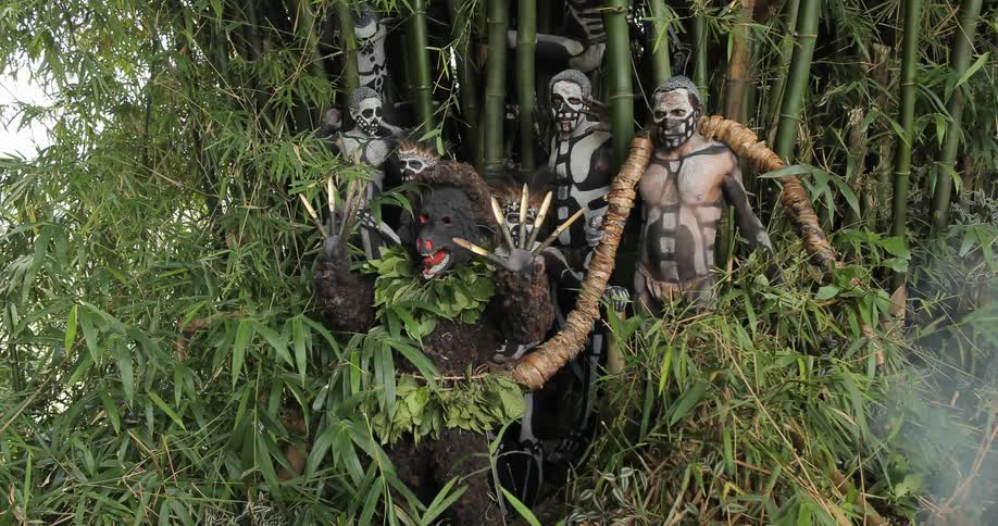 Painted tribesmen standing near a man in a costume