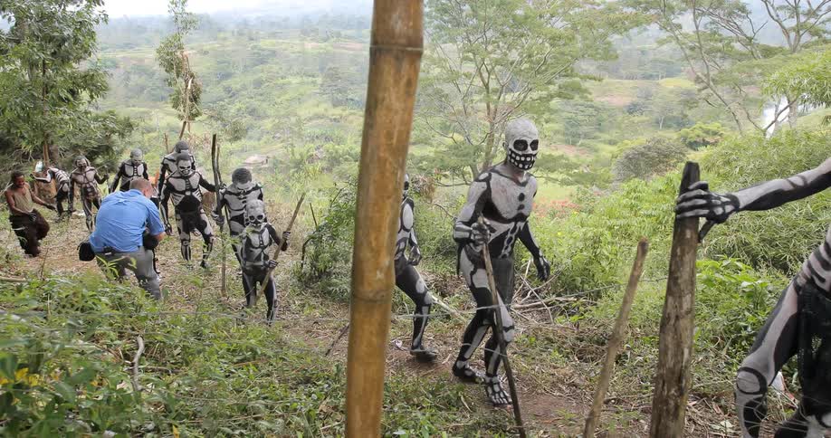 Indigenous men in skeleton paint are photographed as they walk on a path
