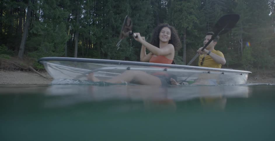 A couple paddles a glass bottom canoe on a lake
