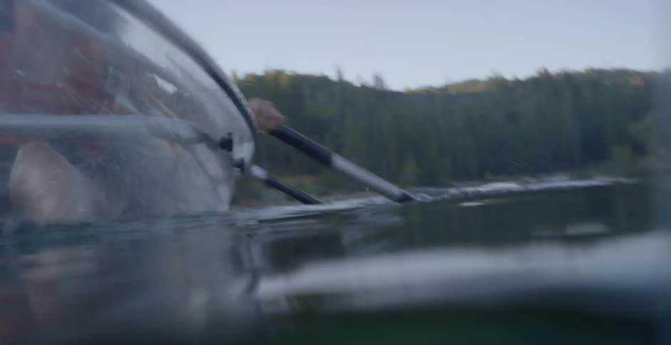 A woman and a man rowing a clear transparent canoe through a lake