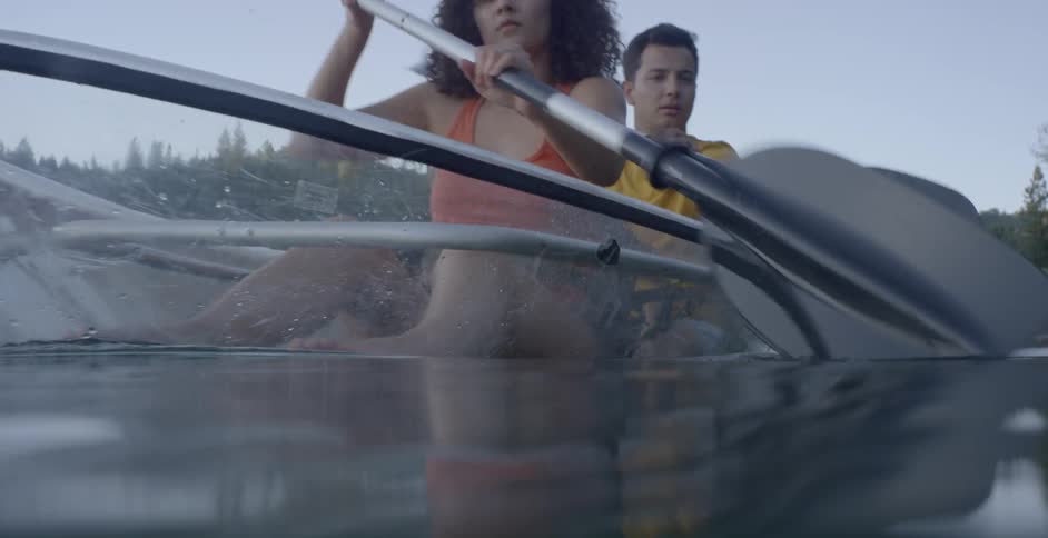 A man and a woman paddling in a see through boat