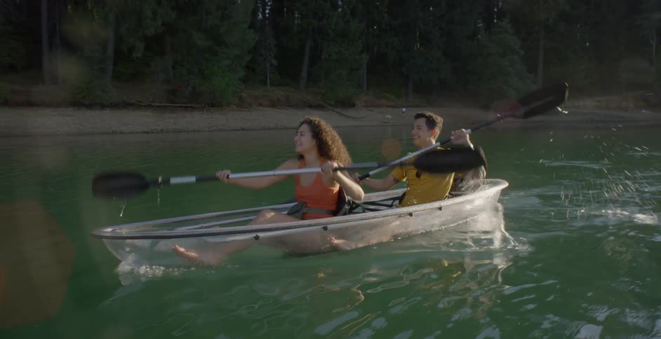 A man and woman rowing a clear canoe through bluegreen water