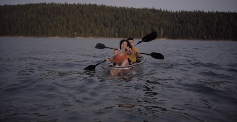 A man and a woman paddle a rowboat across a lake