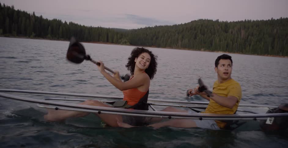 Two people using paddles to row a small boat in a lake surrounded by forest