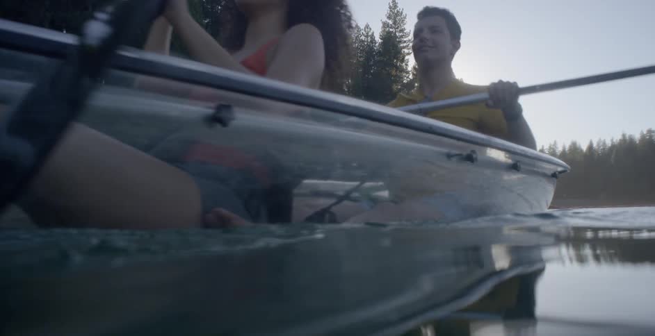 A young man and woman row a boat across a lake