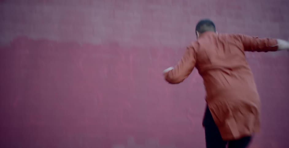 A young man breakdancing outdoors near a red wall during the day