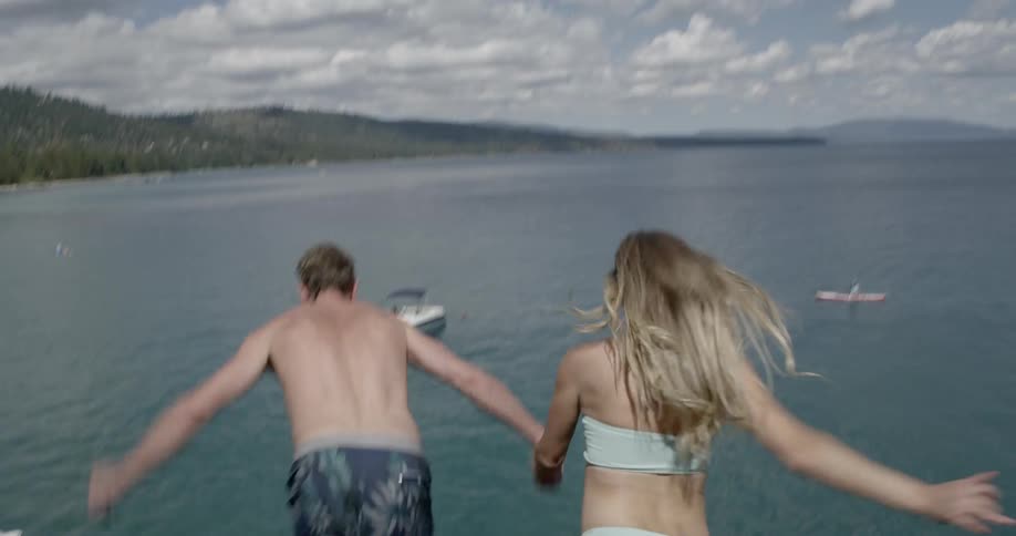 Woman and man jump off a high cliff holding hands during daylight