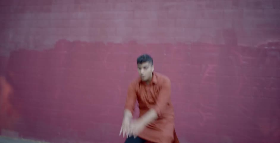 A man dancing freestyle in a shaded area of a car park