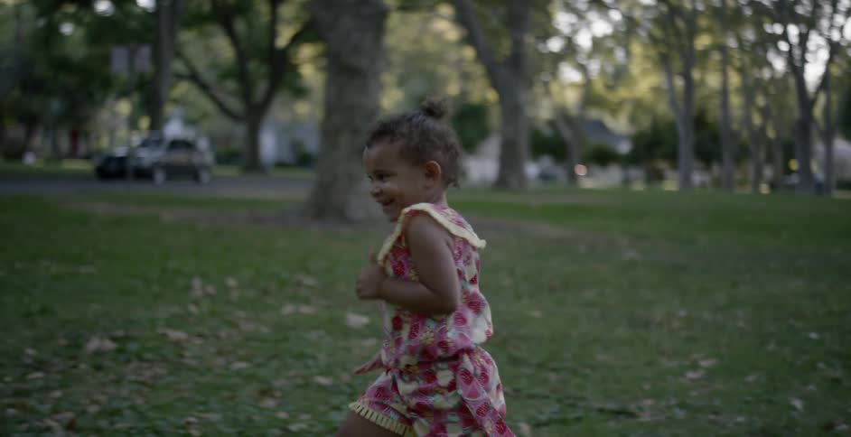 A female toddler running on grass and smiling