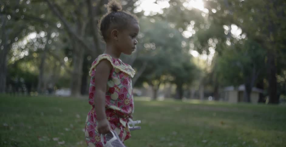 A young girl carries her sandals across the grass