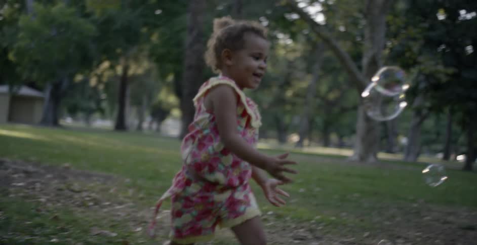Young girl jumping and bursting bubbles outdoors near sunset