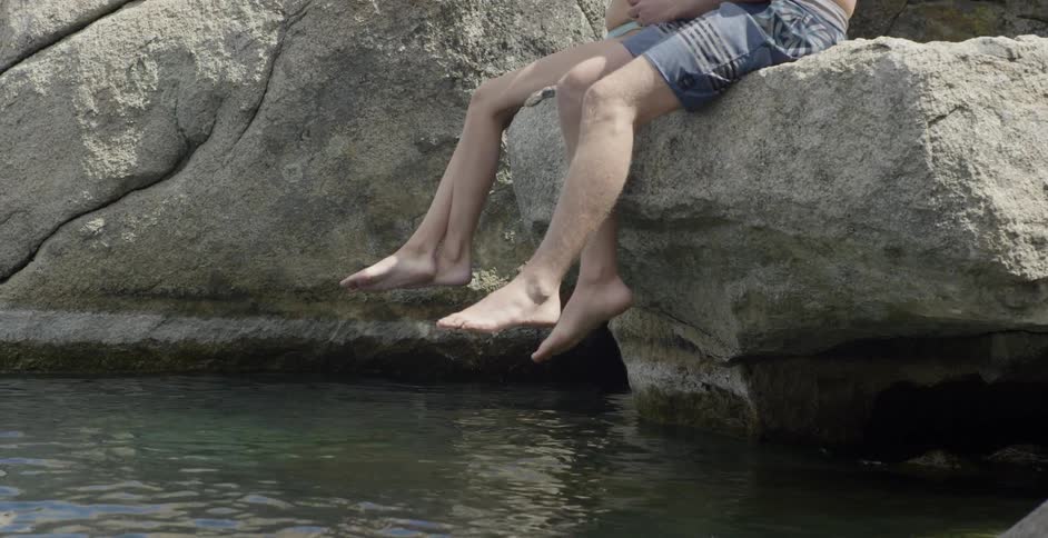 Two people sit on the rocks by the water