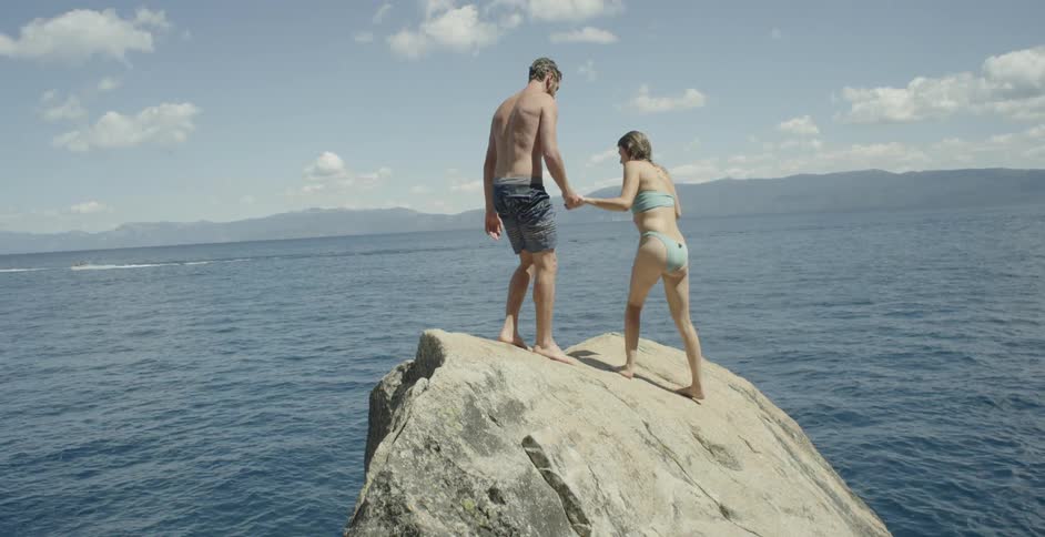 A man helping a woman to climb a rock next to the ocean