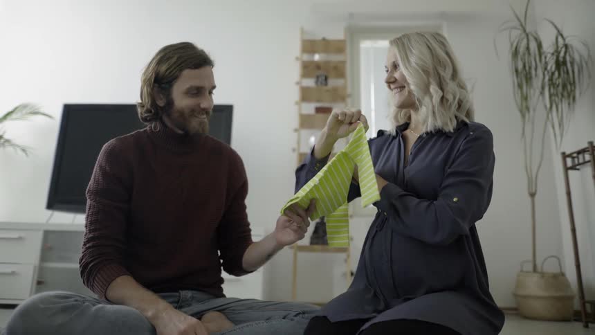 A man and a woman looking a clothing for a baby in the sitting room of a house