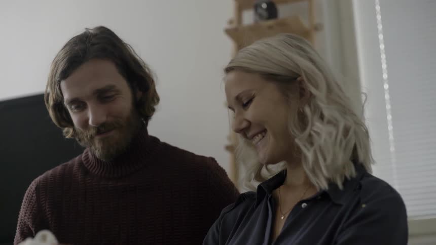 A white woman and a white man hold up babys clothing and smile at one another