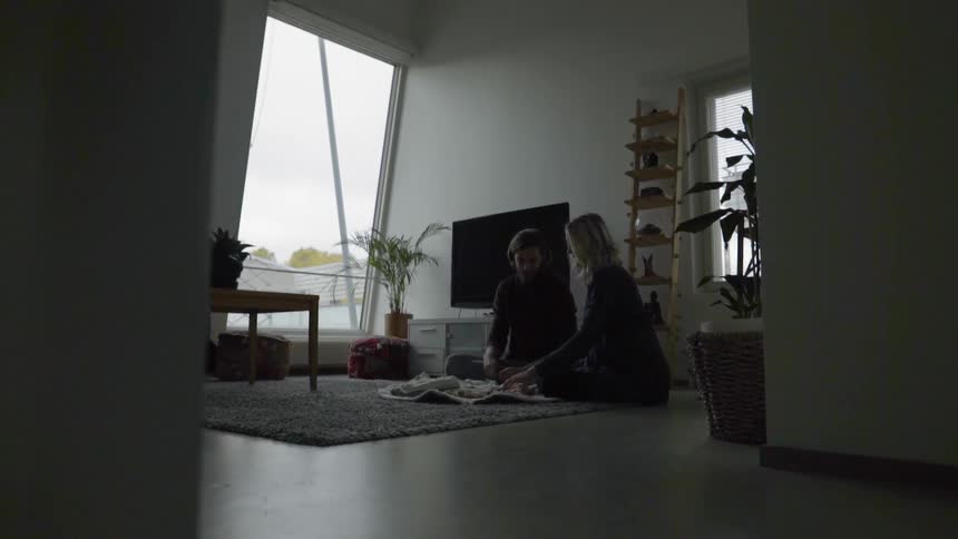 A man and a woman sitting on the floor looking at baby clothing