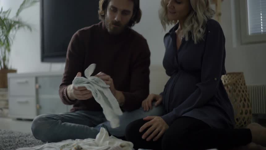 Bearded long hair man and blonde woman sit cross legged on the floor in the living room checking out clothes during daylight
