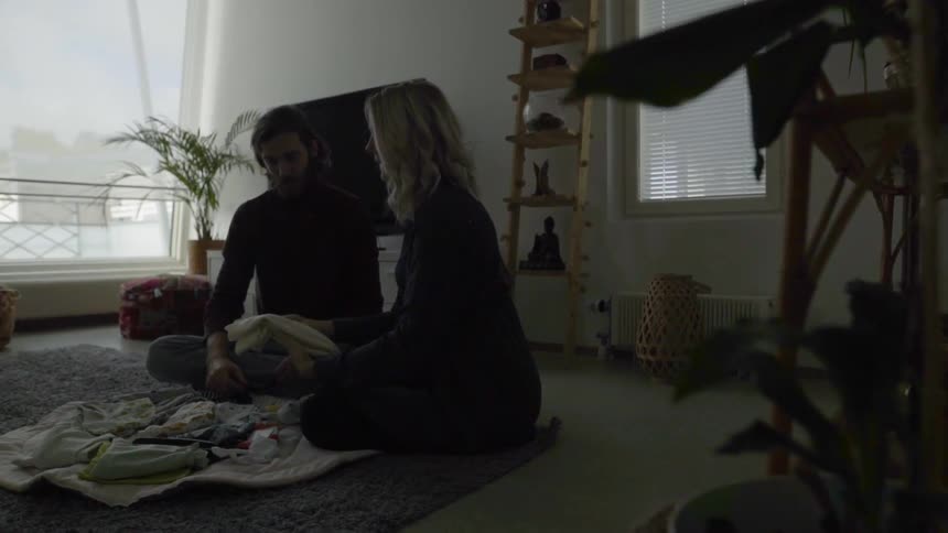 A man and a woman sit on a rug in a living room and fold laundry