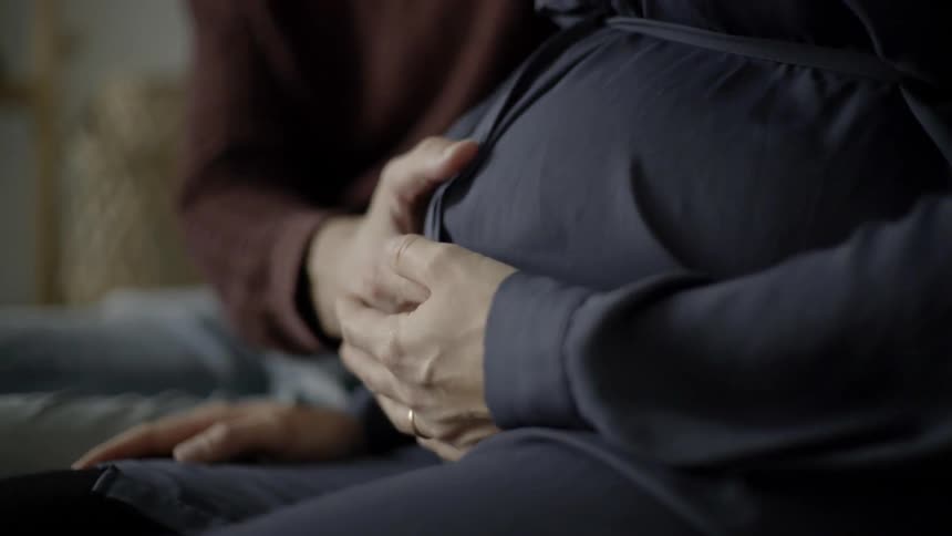 A man and woman hold hands and rub her pregnant belly