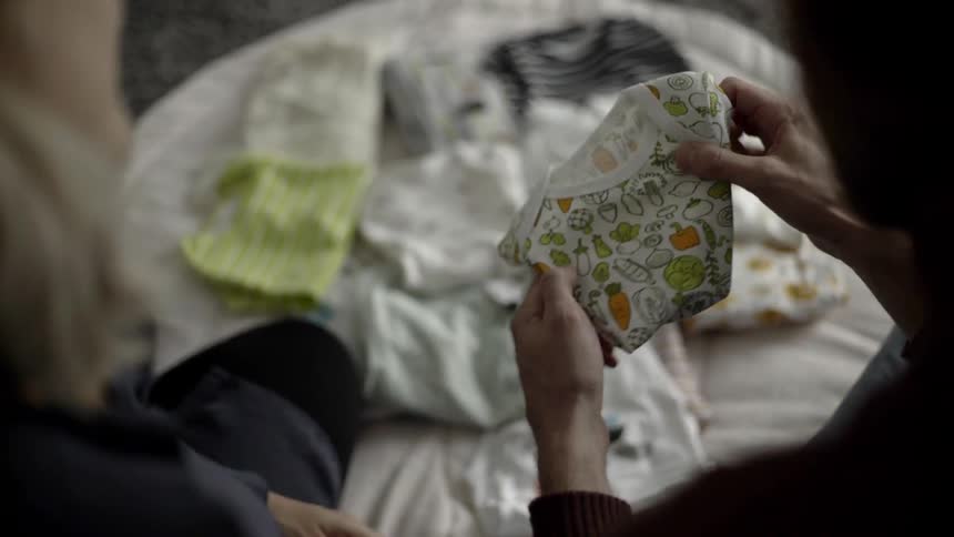 A man and woman sitting on a carpet looking a clothing for a baby