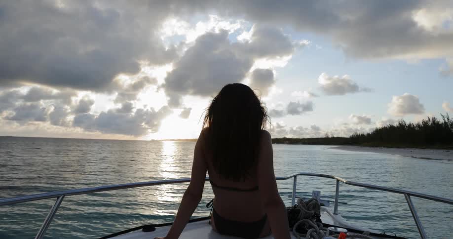 A woman in a bikini sitting on the deck of boat with her legs hanging through the railing