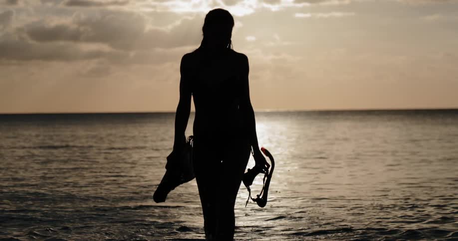 Silhouette of woman walking out of the ocean from snorkeling at sunset
