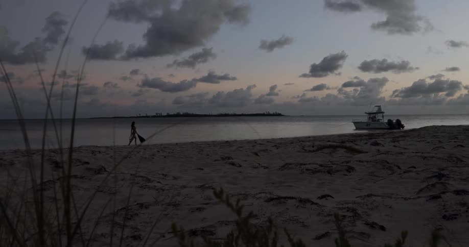 A female walking alone on a beach near a boat