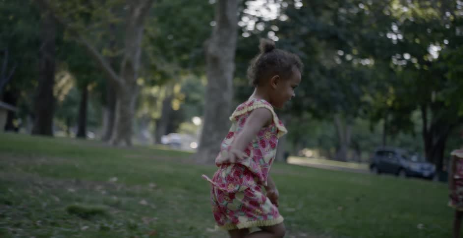 A young girl running after bubbles on a lawn by her twin sister and an adult