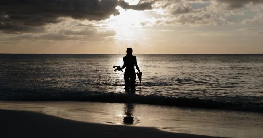 A woman walks out of the ocean and onto a beach
