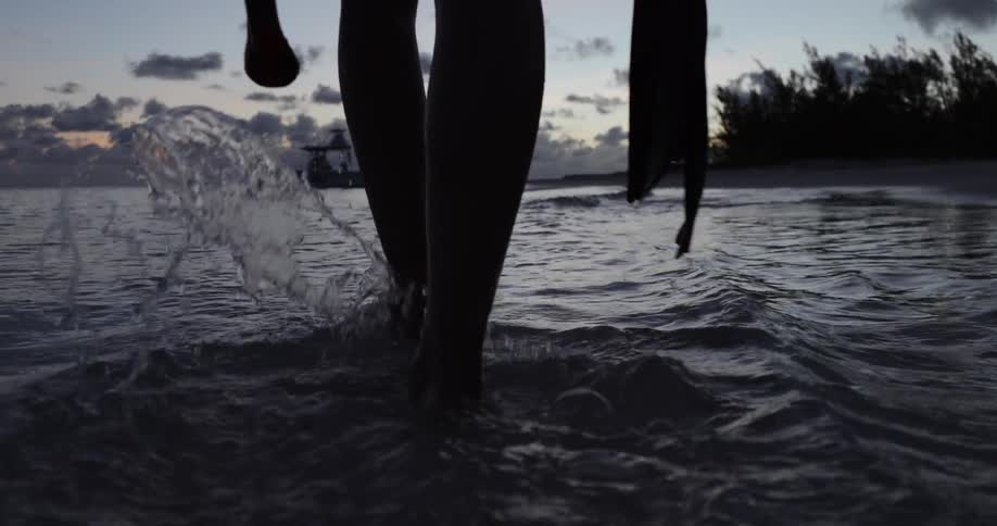 A female holding snorkeling gear walking on a beach towards a boat