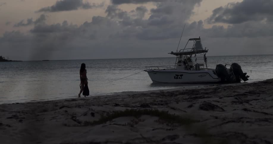 A woman strolls across the shore to a boat