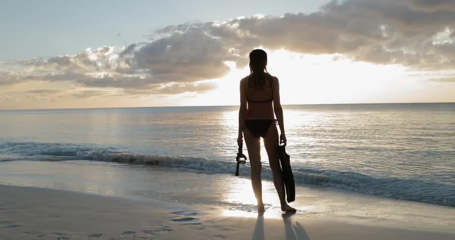 Woman stand on beach holding flippers and snorkel mask
