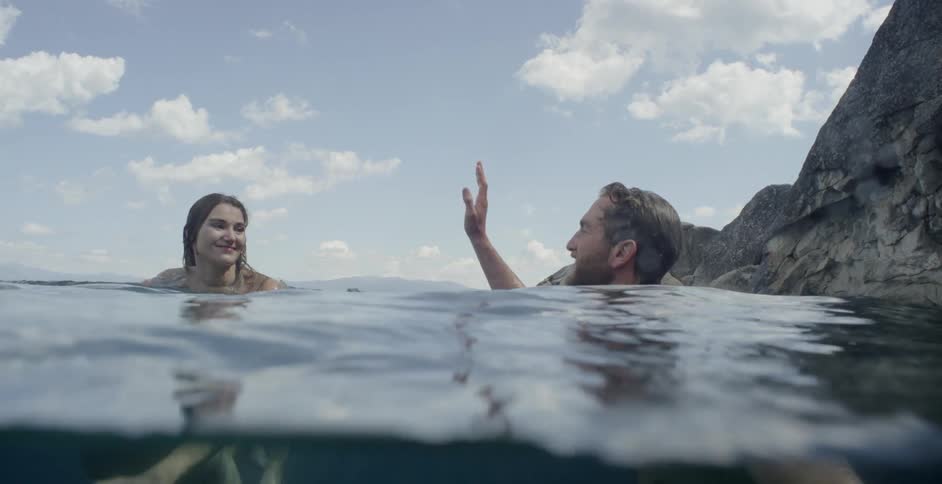A man and woman treading water by a large cliff