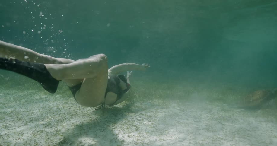 A woman is diving and touching the bottom of the water as she swims