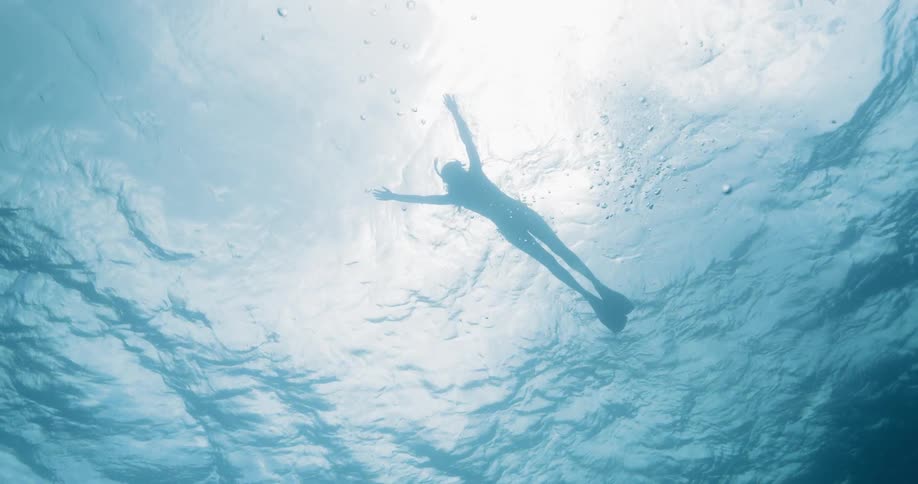 A swimmer in a snorkeling mask and flippers swimming near the surface of a body of water