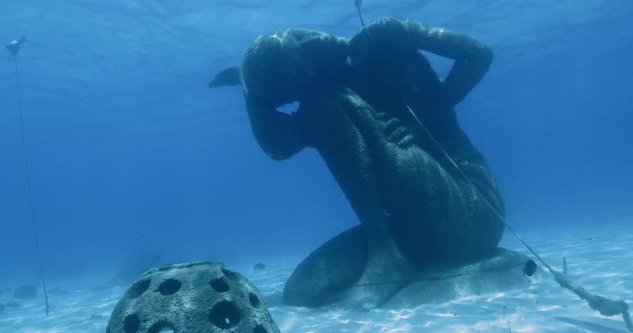 A statue of a kneeling human beneath blue water