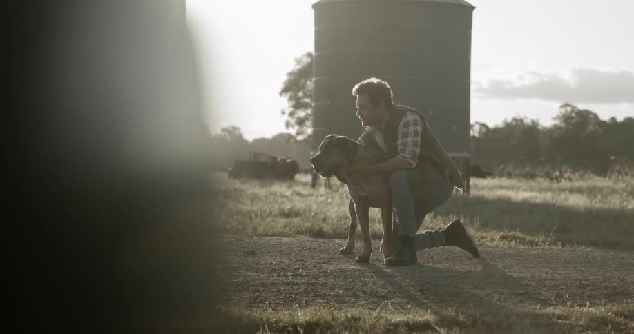 A white male kneels while petting a large dog on a farm