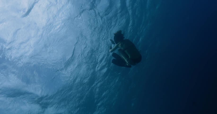 A swimmer wearing flippers and full face goggles does a somersault underwater