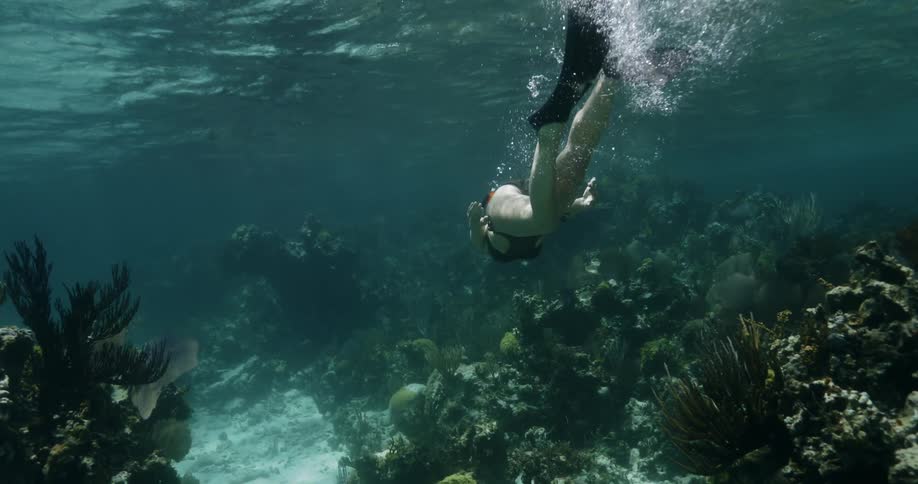 A white female diver swims over coral reefs in the ocean