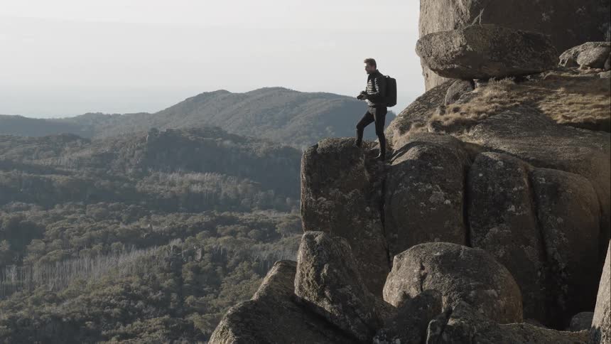 A man stands on top of a mountain and takes pictures