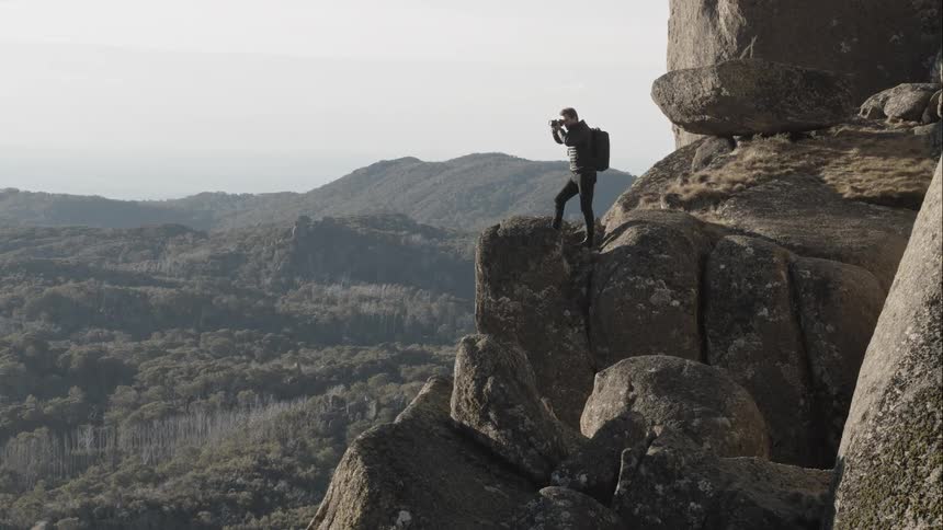 Aerial shot of a man standing on a mountain ridge taking a photo