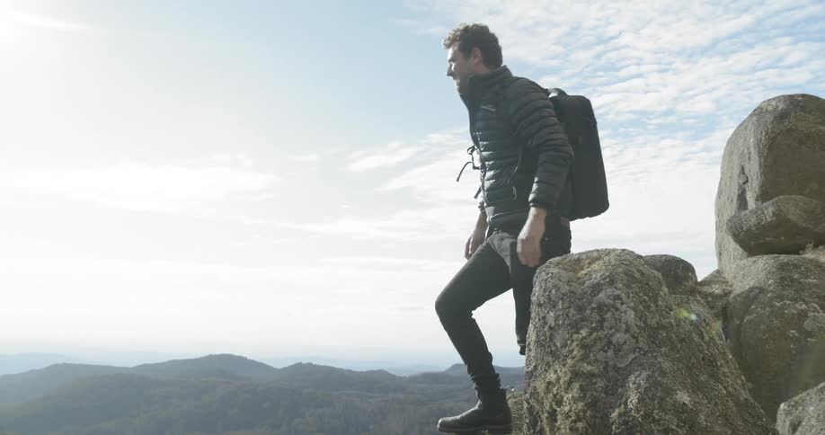 A man climbs to the top of a mountain and looks over the side