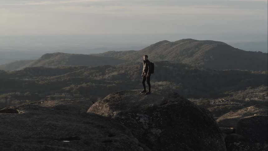 A man climbing and standing atop a boulder on a mountain