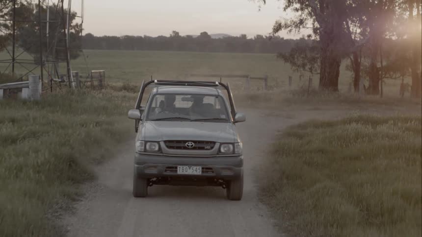A truck with two people inside driving down a dirt road in sunset