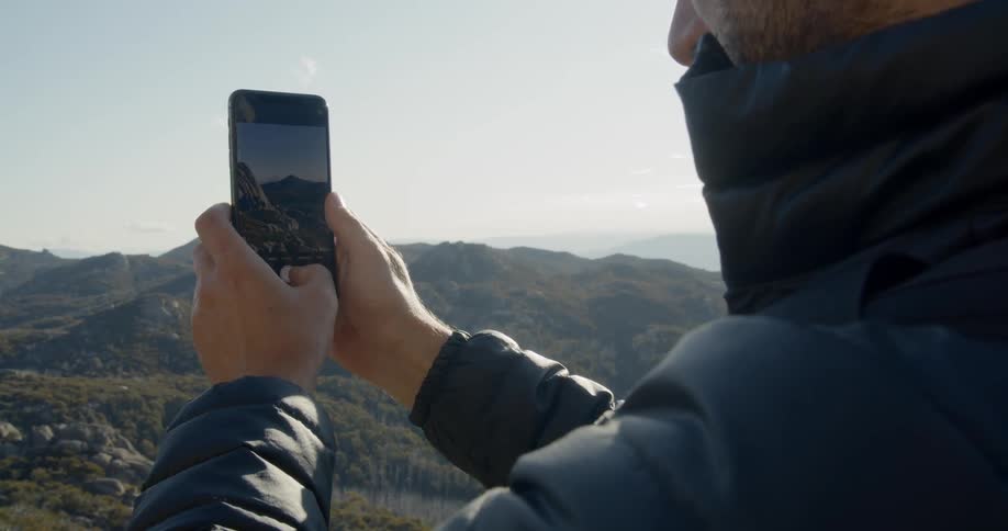 A person is near a mountain area taking photos with his cell phone