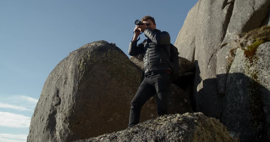 A man taking a photo with a camera on a cliff