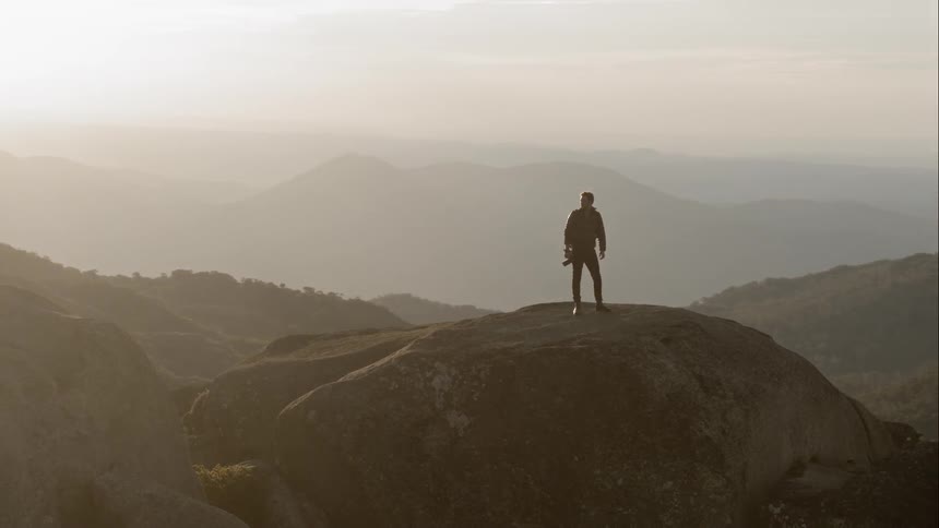 A man climbs up a large rock and stands on to mound
